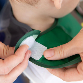 Close-up of hands adjusting the hook-and-loop closure of a Bumkins Caped SuperBib®: The Legend of Zelda™ Link around a child's neck.