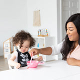 A woman feeds a curly-haired toddler with a Bumkins Silicone Dipping Spoons: Minnie Mouse (Black and Pink) from a pink bowl at a table.