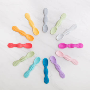 Bumkins Silicone Dipping Spoons 3 Pack: Tutti-Frutti lays flat on a marble background with other colorful spoons in a circular pattern.
