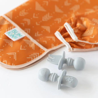 Bumkins Silicone Chewtensils®: Gray sit in front of an orange sleeved bib on a white background; one sits face-down, showing sensory bumps.