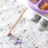 A floral mat with a Bumkins Silicone Chewtensils®: Lavender sits under a high chair; a child's shoes and a divided plate are blurred above.
