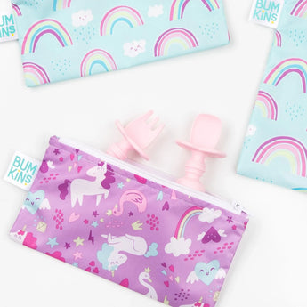 Bumkins Silicone Chewtensils®: Pink peek out of a purple unicorn-print pouch, with two rainbow-print pouches nearby on a white background.