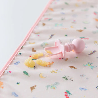 Close-up of a Bumkins Silicone Chewtensils®: Pink with applesauce splatter on a pink waterproof mat on a white background.