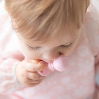 Close-up of a baby in a pink bib chewing a Bumkins Silicone Chewtensils®: Pink.
