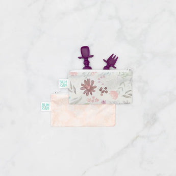 Bumkins Silicone Chewtensils®: Purple peeks from a floral zippered pouch, with another pink pouch underneath on a marble background.