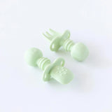 Bumkins Silicone Chewtensils®: Sage rests on a white background; one lays face-down, showcasing the sensory bumps on the back.