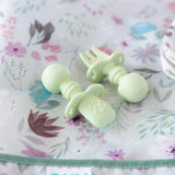 Close-up of Bumkins Silicone Chewtensils®: Sage laying on a purple floral bib; one lays face-down, showing sensory bumps on the back.