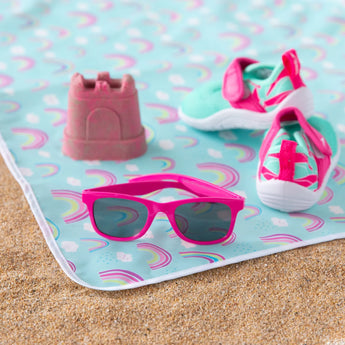 Close-up of Bumkins Splat Mat: Rainbows on sand, with water shoes, pink sunglasses, and a toy on top.