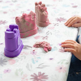 Close-up of a child playing with a purple sandcastle mold and kinetic sand on a Bumkins Splat Mat: Floral.