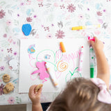 Aerial view of a child drawing with colorful pens on Bumkins Splat Mat: Floral, nibbling a cookie.