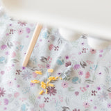 Bumkins Splat Mat: Floral lays under a high chair, covered in macaroni and cheese with a gray silicone utensil nearby.