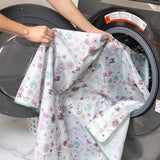 A person places a Bumkins Splat Mat: Floral into an open front-loading washing machine.