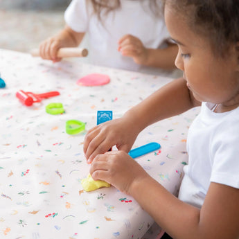 Two kids mold colorful clay on a table covered with Bumkins Splat Mat: Princess Magic for easy cleaning.