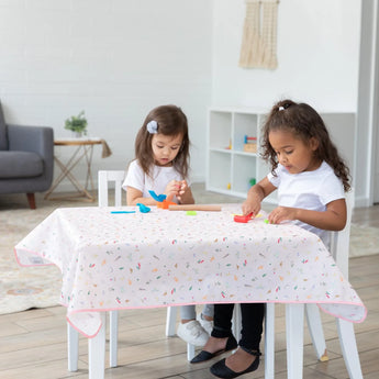 Two girls play with clay at a table covered by Bumkins Splat Mat: Princess Magic for easy cleaning.