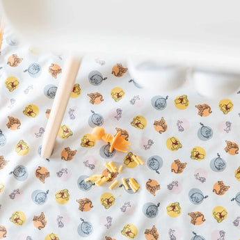 Bumkins Splat Mat: Winnie and Friends lays under a high chair, with an orange baby fork and mac & cheese on top.