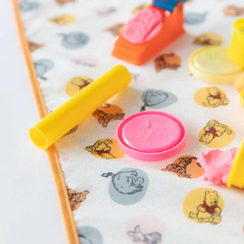 Close-up of colorful modeling clay tools and shapes on Bumkins Splat Mat: Winnie and Friends on a white background.