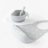 Bumkins Silicone Bib: Hearts rests in front of a gray bowl & spoon set on a white background.