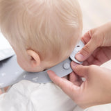 Adult hands fasten the closure of a Bumkins Silicone Bib: Hearts around a baby's neck over a white shirt.