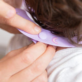 Close-up of hands adjusting the closure of a Bumkins Silicone Bib: Rainbows around a toddler's neck.