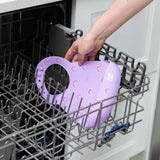 A person places Bumkins Silicone Bib: Rainbows in the top rack of an open dishwasher.