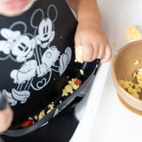 Close-up of a child wearing a Bumkins Silicone Bib: Mickey + Minnie Mouse, with focus on scrambled eggs in the front pocket.