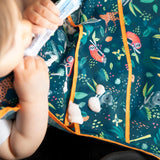 A child enjoys yogurt from a tube, while drops fall onto a Bumkins Super-Sized SuperBib®: Jungle.