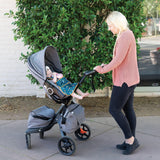 A woman pushes a stroller outdoors with a baby wearing a Bumkins Super-Sized SuperBib®: Jungle.