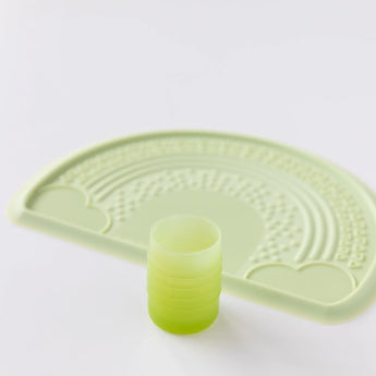 Bumkins Silicone Starter Cup: Sage sits in front of a green placemat on a white background.