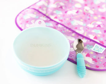 Bumkins Silicone Stretch Lid for Grip Bowl covers a blue bowl next to a blue spoon and purple bib on a white background.