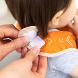 Hands fasten the hook-and-loop closure of an orange Bumkins Starter Bib 2 Pack: Sunshine and Grounded around a child's neck.