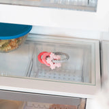 Close-up of a glass refrigerator shelf with a Bumkins Silicone Teething Charms: Pink beside a covered bowl of food.
