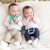 Two babies sit on a plush, cream-colored blanket with teething rings, including Bumkins Silicone Teething Rings 4 Pack: Spring.