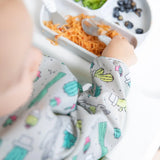 Close-up of a baby in a Bumkins Sleeved Bib: Cacti reaching for spaghetti on a gray plate with a spoon.