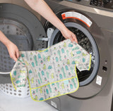 A person holds Bumkins Sleeved Bib: Cacti in front of a front-loading washing machine.