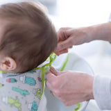 Adult hands adjust the ribbon closure of a Bumkins Sleeved Bib: Cacti around a child's neck.