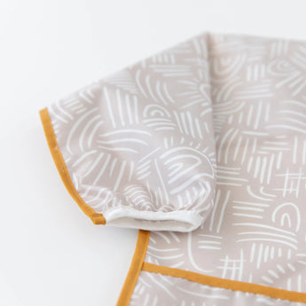 Close-up of Bumkins Sleeved Bib: Wander on a white background, with focus on the white elastic cuff on the sleeve.