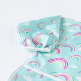 Close-up of Bumkins Sleeved Bib: Rainbows on a white background, with focus on the white elastic cuff on the sleeve.