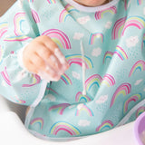 Close-up of a child in a Bumkins Sleeved Bib: Rainbows with a drop of yogurt spilling down the front of the bib.