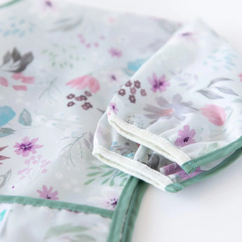 Close-up of Bumkins Sleeved Bib: Floral folded neatly on a white background, with focus on the white elastic cuff on the sleeves.