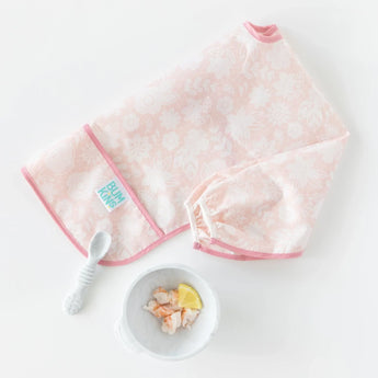 Bumkins Sleeved Bib: Lace lays folded next to a white spoon and a white bowl with shrimp and lemon on a white background.