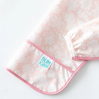 Close-up of Bumkins Sleeved Bib: Lace folded on a white background, with focus on the front pocket and white elastic cuff on the sleeves.