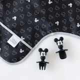 Close-up of Bumkins Sleeved Bib: Mickey Mouse Icon Black + White on a white background, with Mickey Mouse-shaped utensils close by.