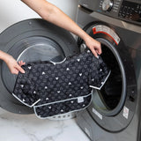 A person holds Bumkins Sleeved Bib: Mickey Mouse Icon Black + White in front of an open front-loading washing machine.