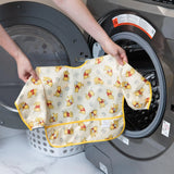 A person holds Bumkins Sleeved Bib: Winnie Loves Hunny in front of an open front-loading washing machine.