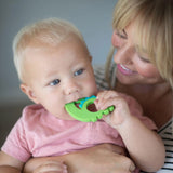 A woman cradles a toddler nibbling on a Bumkins Silicone Teether: Dinosaur.