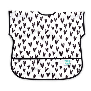 Bumkins Junior Bib: Hearts features a black heart pattern on white waterproof fabric with a black trim, front pocket, and adjustable closure.