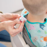 Close-up of hands adjusting the hook-and-loop closure of a Bumkins Junior Bib: Ocean Life around a child's neck.