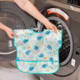 A person holds Bumkins Junior Bib: Ocean Life in front of an open front-loading washing machine.