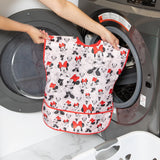 A person holds a Bumkins Short-Sleeved Smock: Minnie Mouse Classic in front of an open front-loading washing machine.