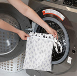 A person holds a Bumkins Wet Bag: Hearts in front of a front-loading washing machine.